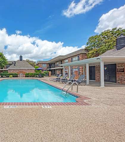 A swimming pool surrounded by a brick building and trees.