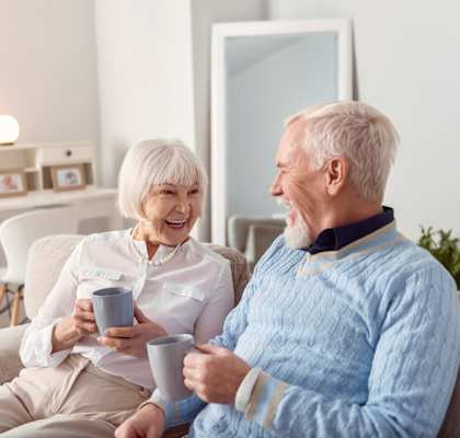 An older couple sitting on a couch holding cups of coffee