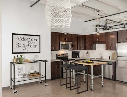 A kitchen with a fridge, stove, and island with a bar stool.