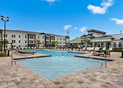 a swimming pool with lounge chairs and buildings in the background at The Enclave at Deer Moss Creek, Niceville