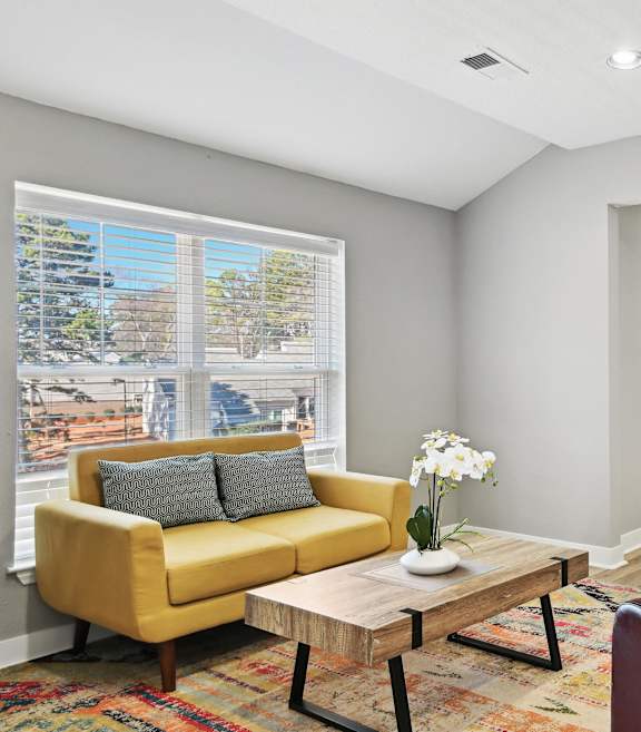A yellow sofa with grey pillows sits in a room with a coffee table in front of it.