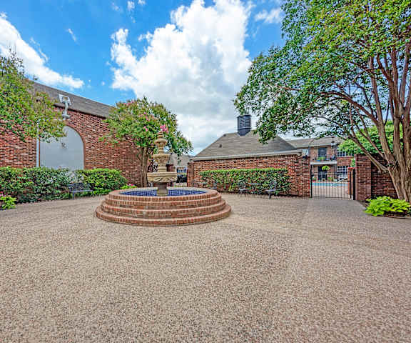 A courtyard with a fountain surrounded by brick walls and trees.