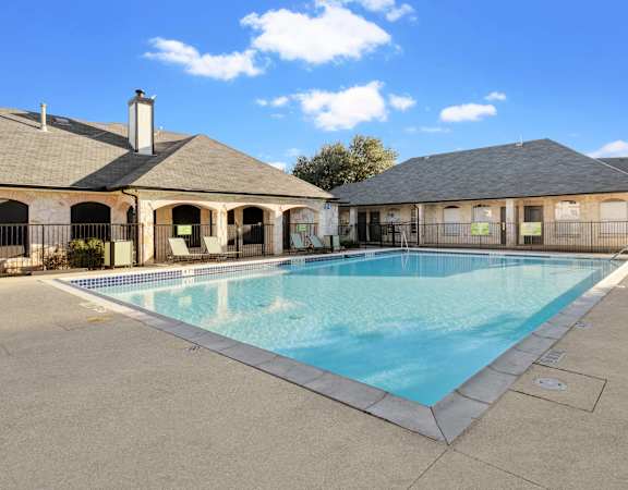 A shimmering pool with an expansive deck, cozy lounge chairs, and a stylish stone-accented clubhouse at Huntington Meadows Apartments.