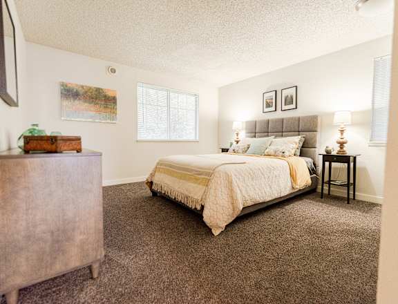 A bedroom with a bed, nightstand, and a painting on the wall at Ellyson Apartment Homes in Tacoma, WA
