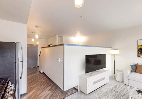 A modern kitchen with a refrigerator, a television, and a white couch.