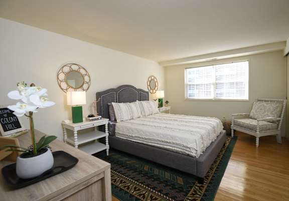 A bedroom with a bed, chair, and a flower vase on a table.