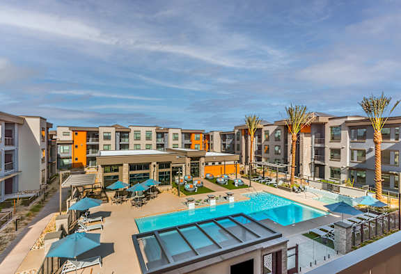 A large swimming pool is surrounded by sun loungers and umbrellas in a sunny courtyard.