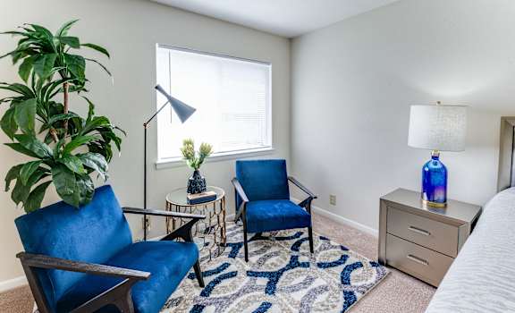 a living room with two blue chairs and a table with a lamp and a window