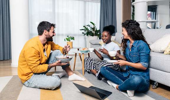 Three people are sitting on the floor eating food.