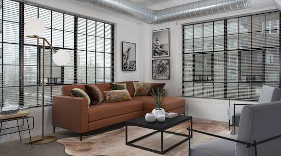 A living room with a brown couch, a black coffee table, and a large window with blinds.