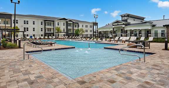 a swimming pool with lounge chairs and buildings in the background at The Enclave at Deer Moss Creek, Niceville