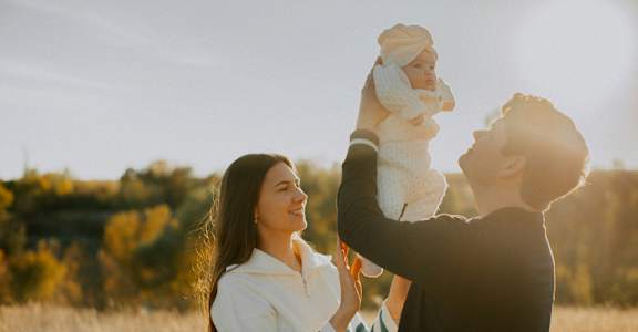 A man holding a baby up in the air while a woman looks on.