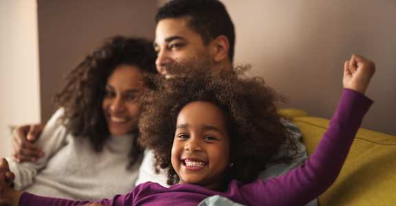 a young girl is sitting on a couch with her parents
