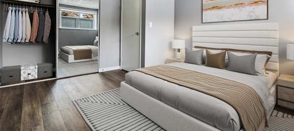 A bedroom with a large bed and a closet with clothes hanging.