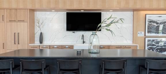 A modern kitchen with a dark countertop and black bar stools.