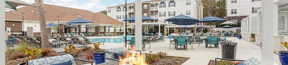 an outdoor patio with a fire pit and chairs and umbrellas at The Met Apartment Homes, Hattiesburg, 39402