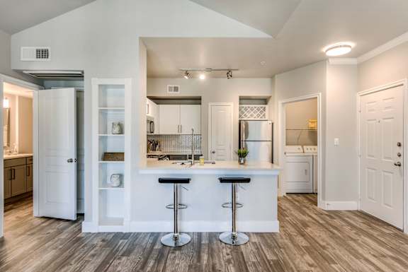 A kitchen with white cabinets and a bar area with two stools.