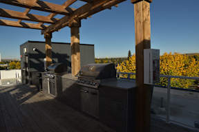 A wooden pergola over a patio with a grill and outdoor kitchen.