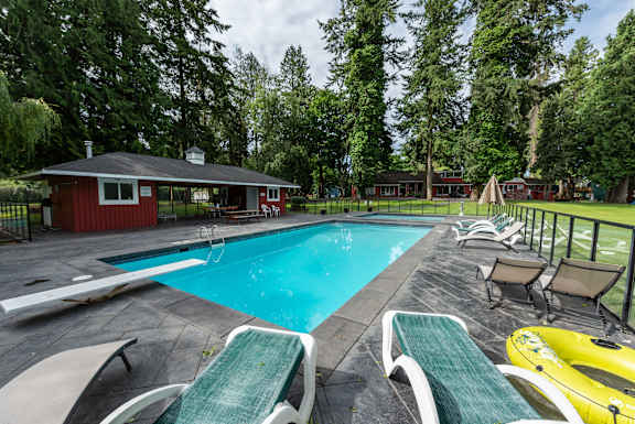 A pool with lounge chairs and a red building in the background.