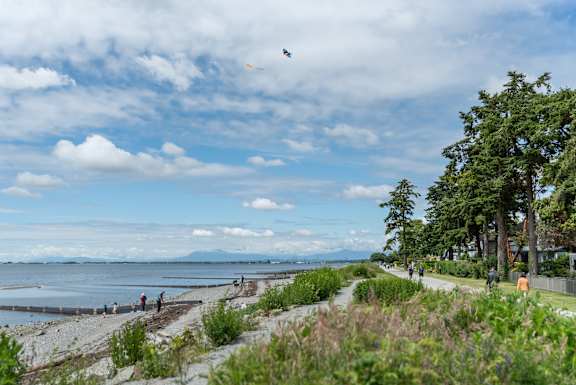 A kite is flying in the sky over a beach with people walking along the shore.