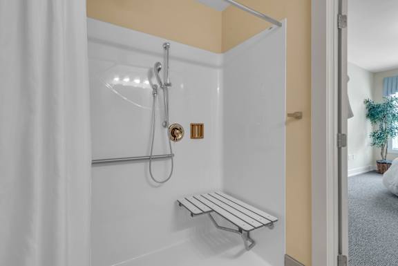 A white shower with a bench and a shower head.