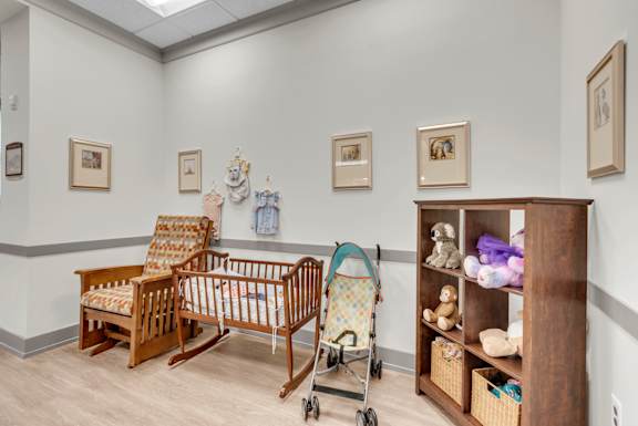 A baby nursery with a rocking chair, crib, and shelf with toys.