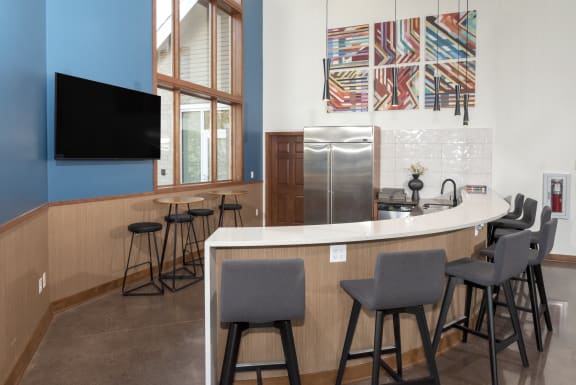 a kitchen with bar stools and a counter with chairs and a tv