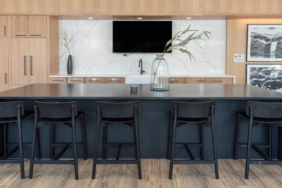 A modern kitchen with a dark countertop and black bar stools.
