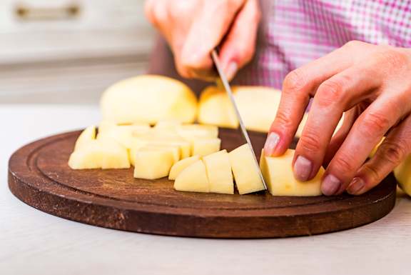 A person cutting a tomato on a wooden cutting board.