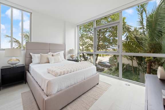 A bedroom with a large bed and a view of the outdoors through the windows.