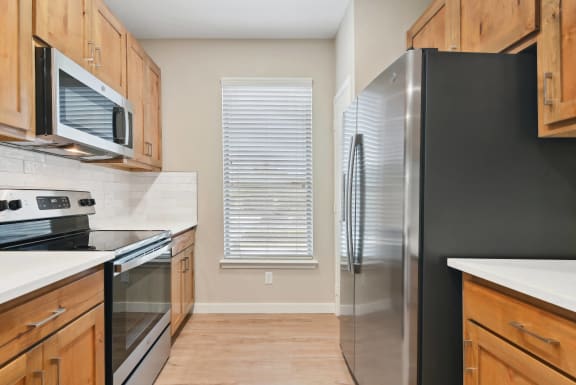 a kitchen with stainless steel appliances and wooden cabinets at The Canyons Apartments, Fort Worth, TX