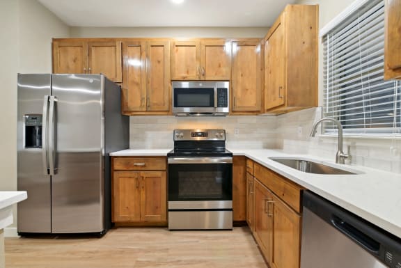 a kitchen with stainless steel appliances and wooden cabinets at The Canyons Apartments, Fort Worth, TX