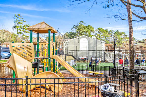 A playground with a yellow slide and a black fence.