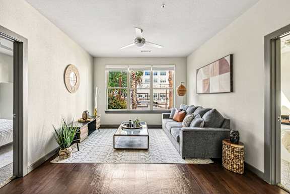 A living room with a grey couch, a coffee table, and a large window.