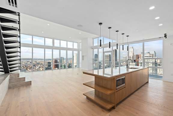 A modern kitchen with a wooden island and stairs leading to the upper level. at Olympic + Hill Apartments, Apartments, Los Angeles, CA