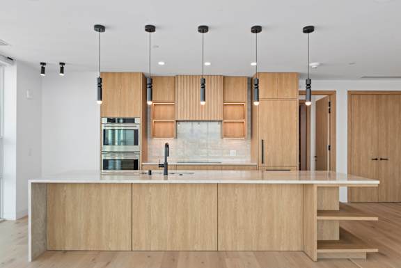 A modern kitchen with wooden cabinets and a white countertop. at Olympic + Hill Apartments, Apartments, Los Angeles, CA