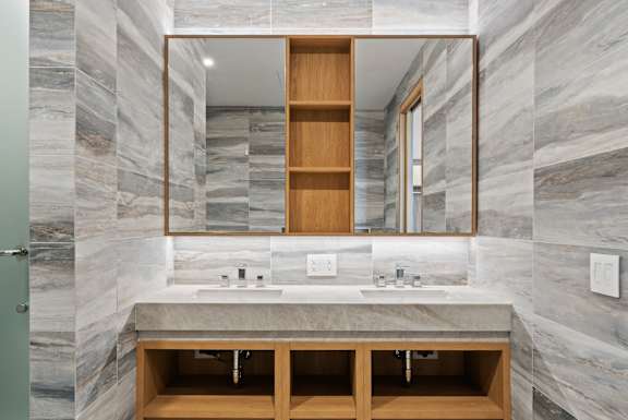 A bathroom with a marble wall and a wooden medicine cabinet. at Olympic + Hill Apartments, Apartments, Los Angeles, CA