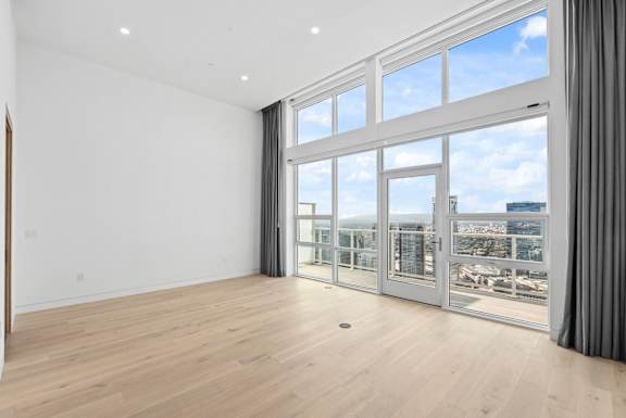 A large, empty room with a view of the city through floor-to-ceiling windows. at Olympic + Hill Apartments, Apartments, Los Angeles, CA
