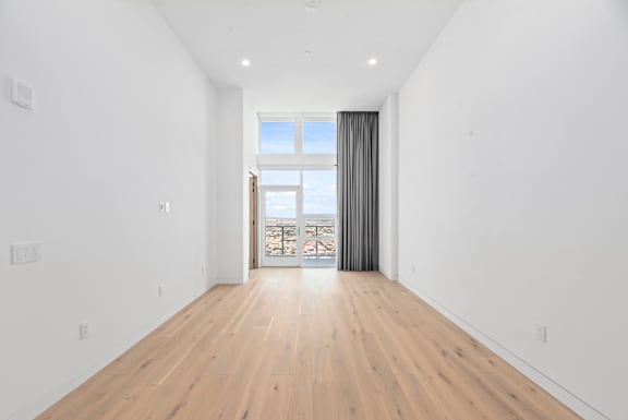 A spacious room with wooden flooring and a large window with curtains. at Olympic + Hill Apartments, Apartments, Los Angeles, CA