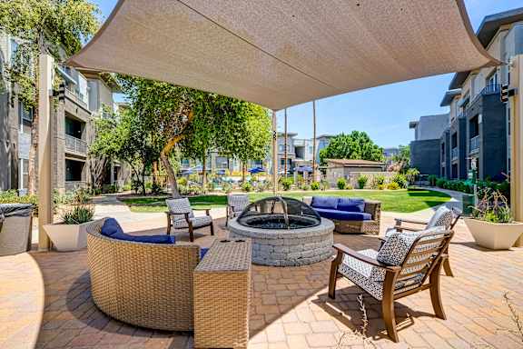 A patio with a fire pit and chairs under a canopy.