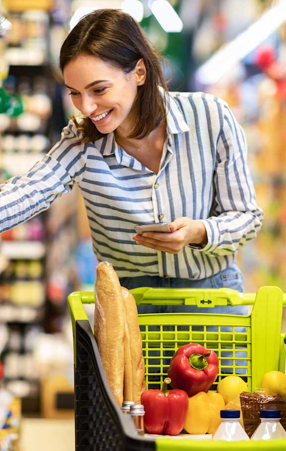 A woman is shopping in a grocery store with a green shopping basket.