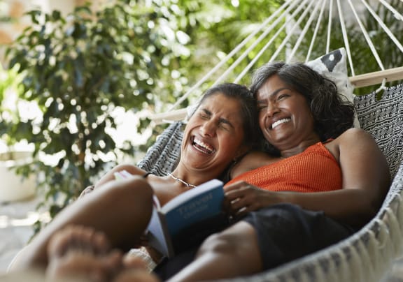 two women laying in a hammock reading a book
