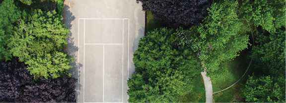 A tennis court is surrounded by green trees.