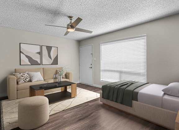 A modern living room with a beige sofa, a coffee table, and a bed with a green blanket.