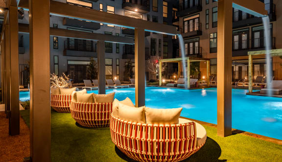 a night time view of the outdoor seating area with the pool and water feature in the background