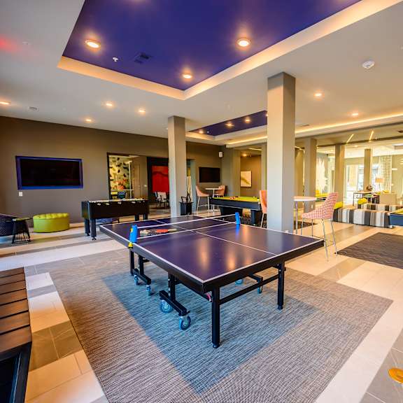 A resident lounge with a ping pong table, pool table, foosball table, other game tables, chairs, and TV at Harmony Luxury Apartments.