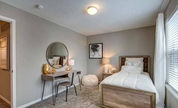 A bedroom with a bed, desk, chair, and a mirror.