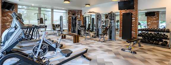 A gym with a variety of equipment including a treadmill, weights, and a television at Penn Circle, Carmel, 46032.