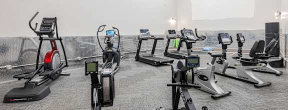 A row of treadmills and stationary bikes are lined up in a gym.