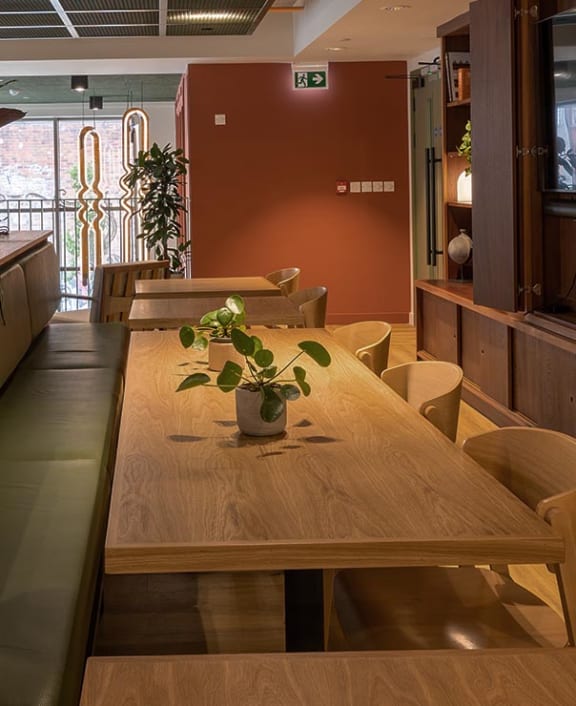 a wooden table in a restaurant with chairs and a plant